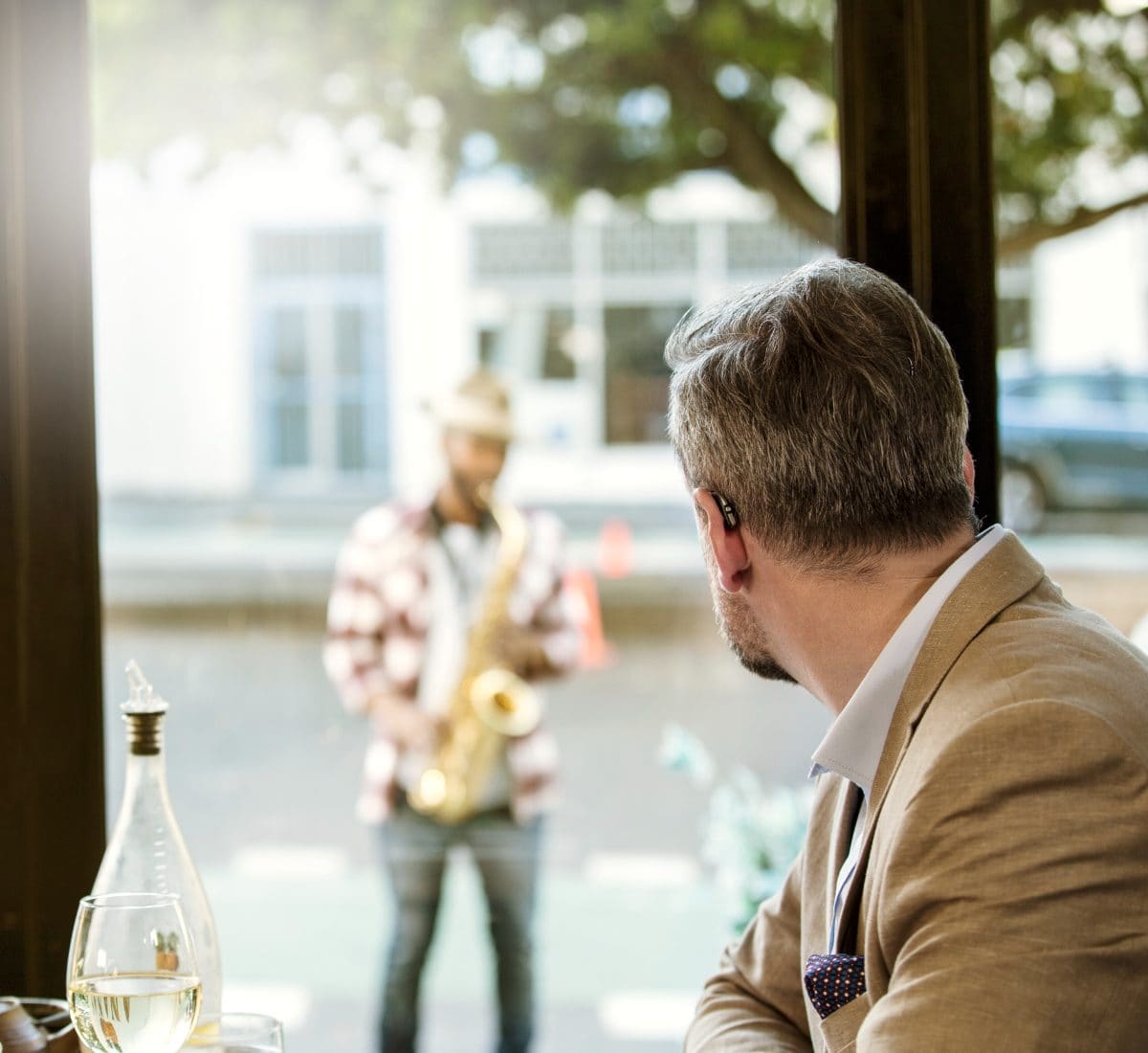 A man at a café table listening to a street musician outside