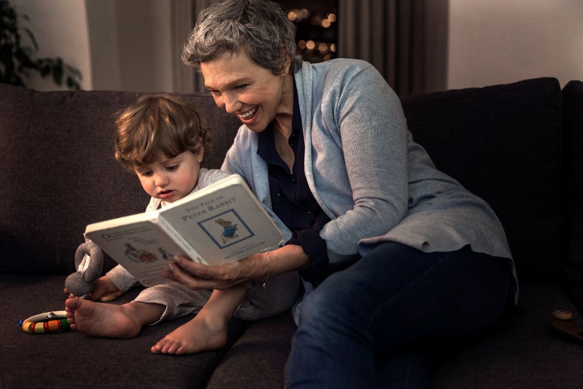 A grandmother wearing hearing aids reads a picture book with her grandchild
